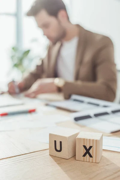 Enfoque selectivo de cubos de madera con letras ux en la mesa y diseñador creativo en el fondo - foto de stock