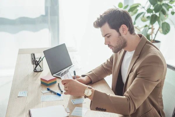 Side view of handsome ux designer working with wireframe sketches for mobile website at table — Stock Photo