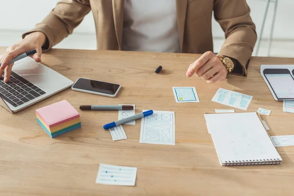 Vue recadrée du concepteur à l'aide d'un ordinateur portable tout en planifiant des croquis pour l'interface d'application mobile à la table — Photo de stock