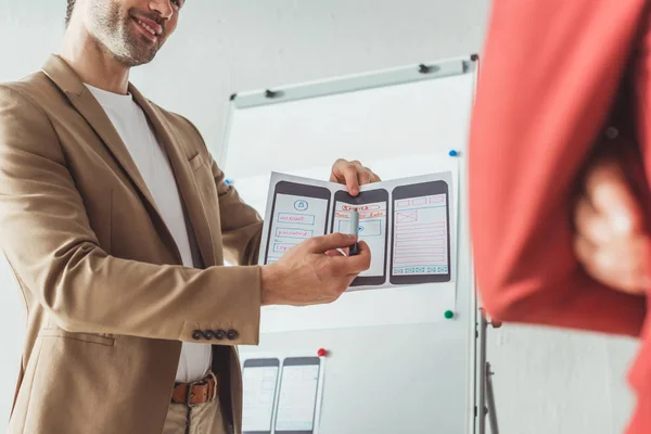 Cropped view of smiling designer presenting wireframe sketches for mobile website to colleague in designer studio — Stock Photo