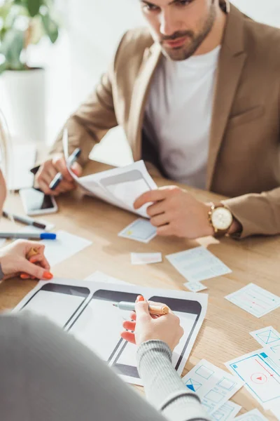 Enfoque selectivo de diseñadores creativos que planifican bocetos de marco de alambre para el sitio web móvil en la mesa - foto de stock