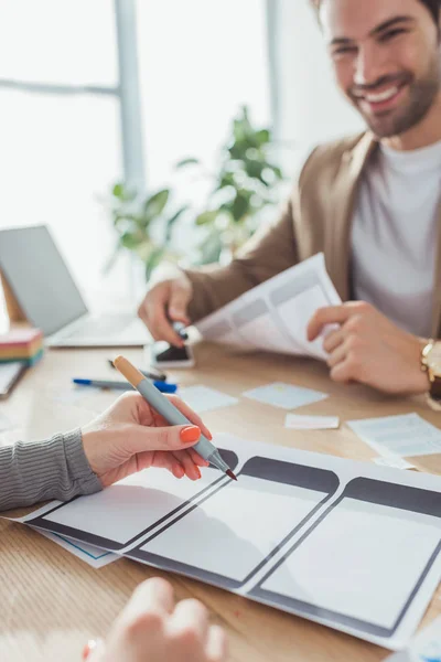 Selective focus of designer noticing on sketch of app interface with smiling colleague at table — Stock Photo