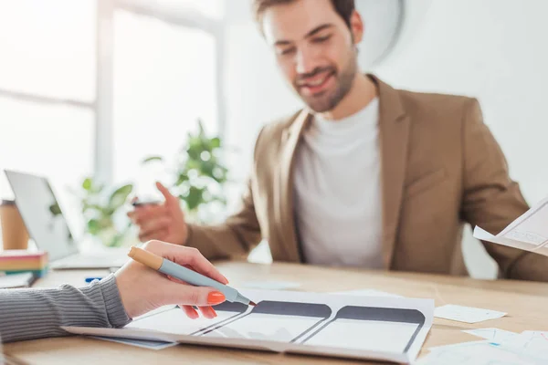 Selective focus of smiling creative designer working with mobile website templates with colleagues at table — Stock Photo