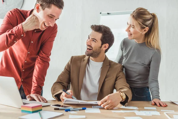 Foco seletivo de designers sorridentes com esboços de wireframe do site no estúdio de designer — Fotografia de Stock