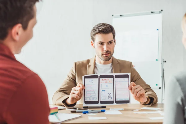 Selective focus of designer showing layout of mobile web prototype to colleagues in office — Stock Photo