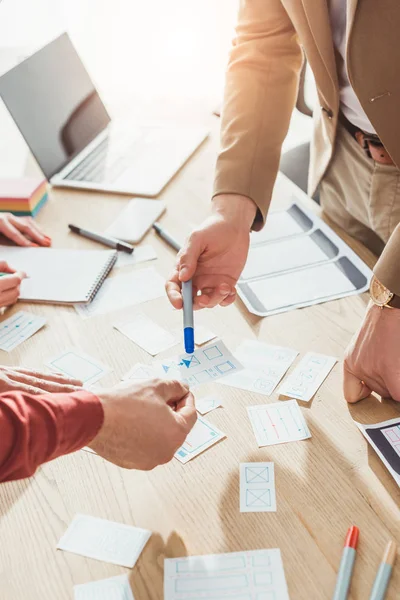 Cropped view of ux designers working with sketches and mobile wireframe layouts at table — Stock Photo