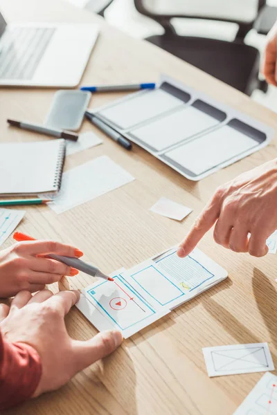 Cropped view of ux designers developing mobile app with layouts on table — Stock Photo