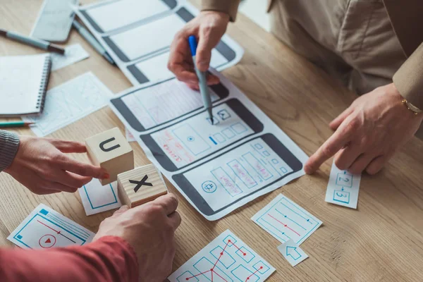 Vista cortada de designers com esboços wireframe site móvel e cubos com letras ux na mesa — Fotografia de Stock