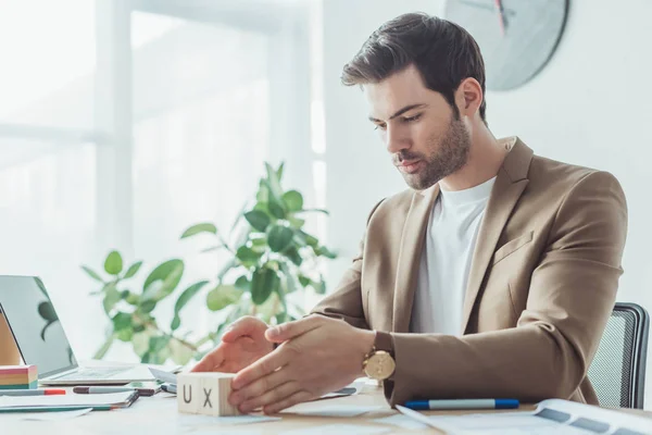 Side view of creative designer holding wooden cubes with ux letters at table in office — Stock Photo