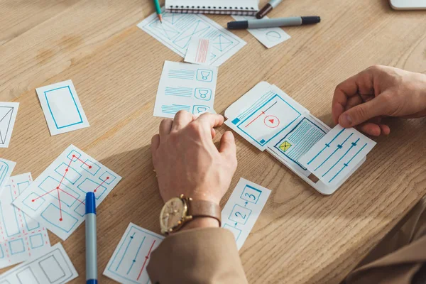 Cropped view of ux designer planning mobile website design with layouts on table — Stock Photo