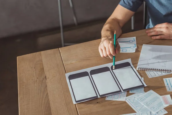 Vista recortada del diseñador que desarrolla el diseño del sitio web móvil en la mesa - foto de stock