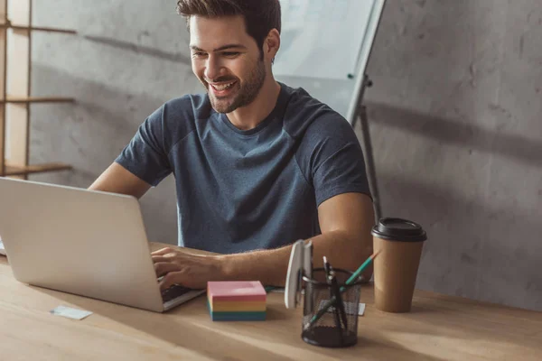 Selective focus of smiling ux developer using laptop by layouts on table — Stock Photo