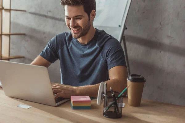 Focus sélectif du développeur souriant ux en utilisant un ordinateur portable par mises en page sur la table — Photo de stock