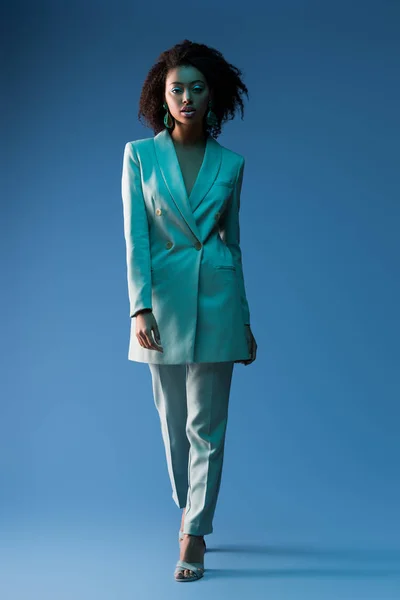 Attraktive afrikanisch-amerikanische Frau im Anzug schaut in die Kamera auf blauem Hintergrund — Stockfoto