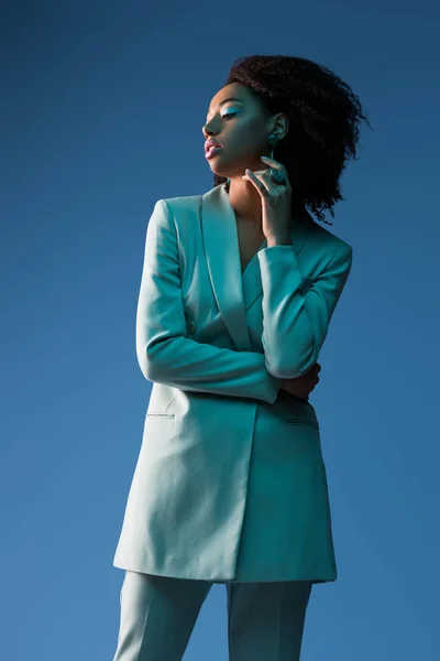 Atractiva mujer afroamericana en traje aislado en azul - foto de stock