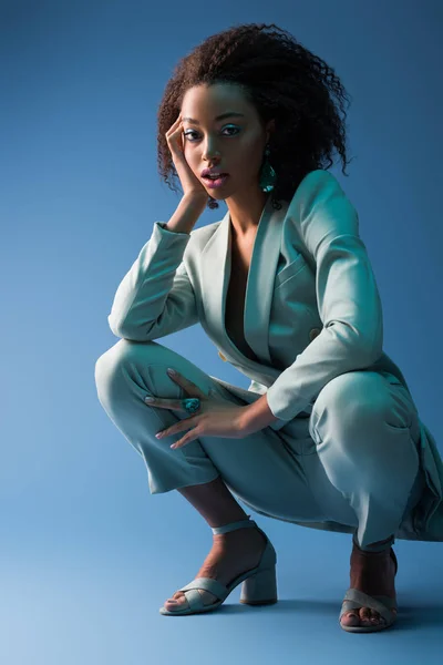 Atractiva mujer afroamericana en traje elegante sobre fondo azul - foto de stock
