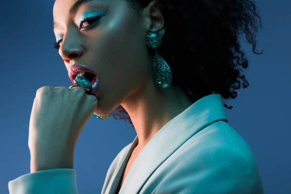 Elegante mujer afroamericana mordiendo anillo aislado en azul - foto de stock