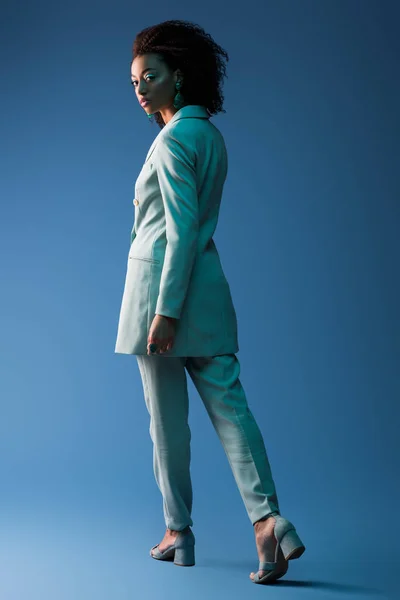 Mujer afroamericana en traje mirando la cámara sobre fondo azul - foto de stock