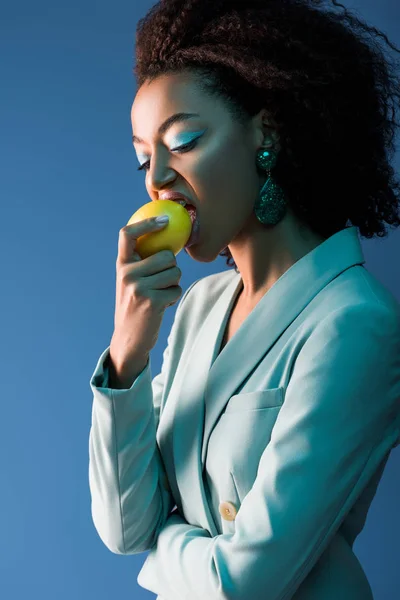 Stylish african american woman with makeup eating lemon isolated on blue — Stock Photo