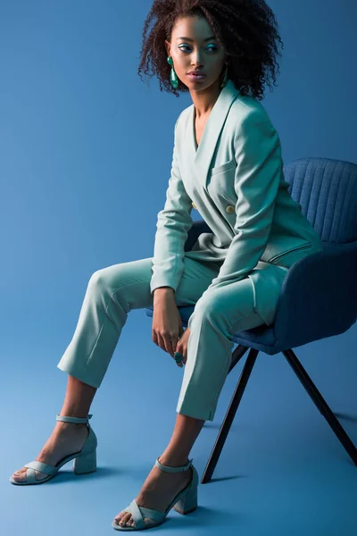 Afrikanische Amerikanerin sitzt auf Sessel auf blauem Hintergrund — Stockfoto