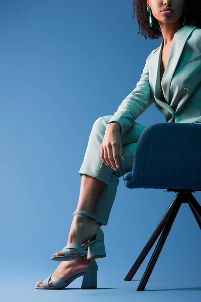 Abgeschnittene Ansicht einer afrikanisch-amerikanischen Frau, die auf einem Sessel auf blauem Hintergrund sitzt — Stockfoto