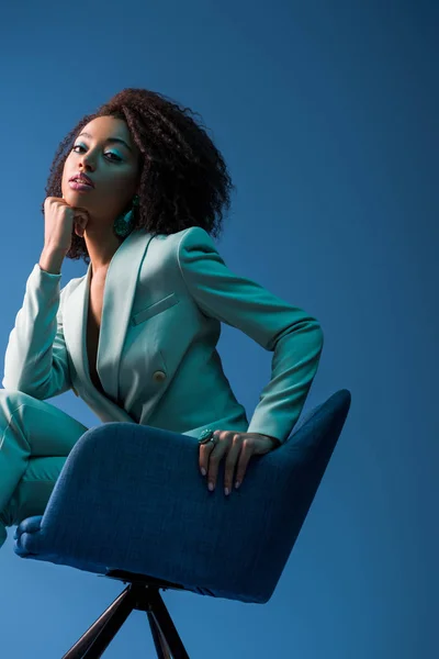 African american woman sitting on armchair isolated on blue — Stock Photo