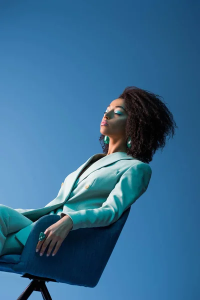 Donna afroamericana seduta su poltrona con gli occhi chiusi isolati sul blu — Foto stock