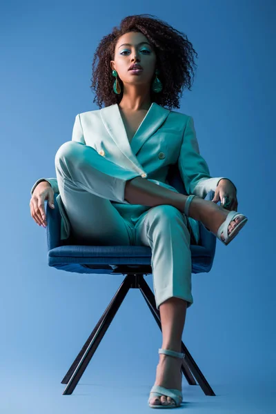 Africano americano mulher sentado em poltrona no fundo azul — Fotografia de Stock