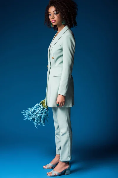 Attractive african american woman holding bouquet on blue background — Stock Photo