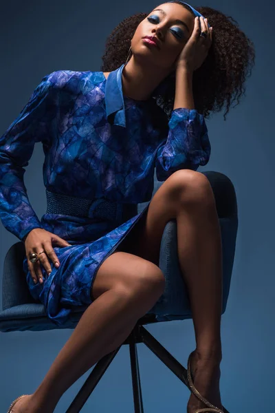 Attrayant afro-américain femme assise sur fauteuil isolé sur bleu — Photo de stock