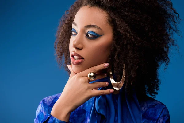 Приваблива афроамериканська жінка з макіяжем в одязі дивиться ізольовано на синьому — стокове фото