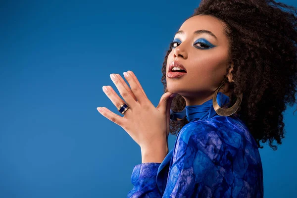 Stylish african american woman in dress with makeup looking at camera isolated on blue — Stock Photo