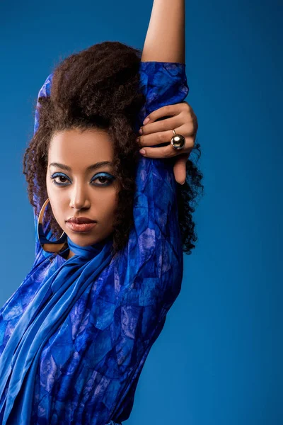 Stylish african american woman in dress looking at camera isolated on blue — Stock Photo