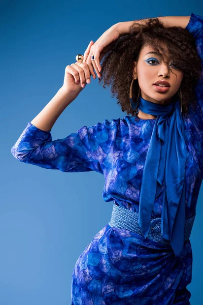 Stylish african american woman in dress looking at camera isolated on blue — Stock Photo