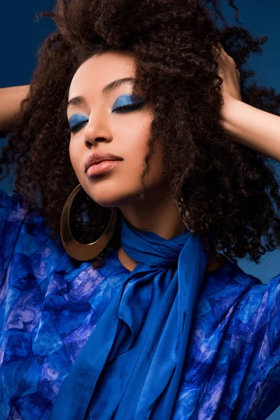Mujer afroamericana con estilo en vestido con los ojos cerrados y maquillaje aislado en azul - foto de stock