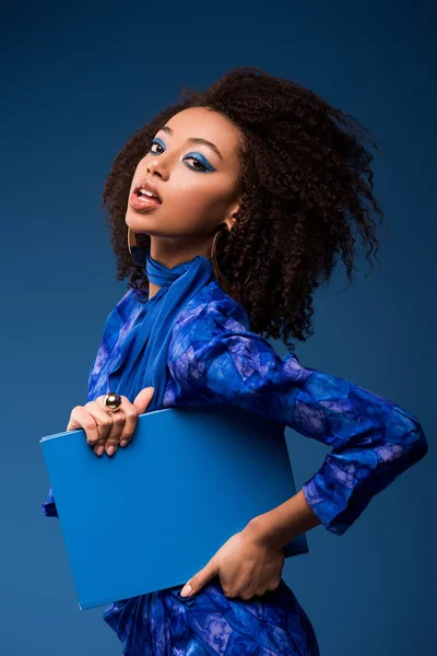 Attraente donna afro-americana in possesso di cartella isolato su blu — Foto stock