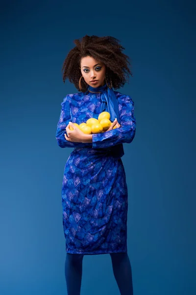 Mulher americana africana atraente segurando limões isolados em azul — Fotografia de Stock