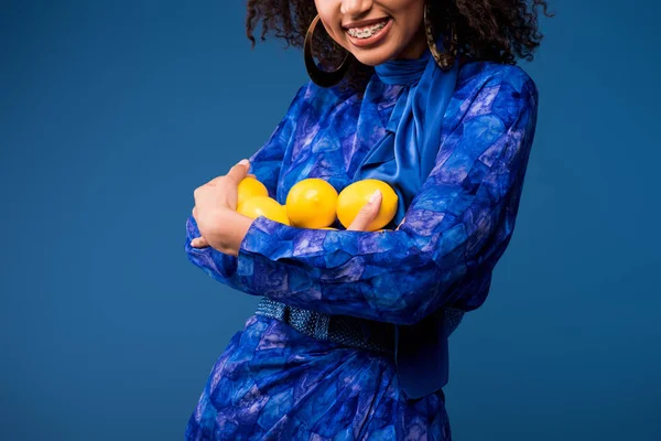 Vista cortada de mulher afro-americana sorridente segurando limões isolados em azul — Fotografia de Stock