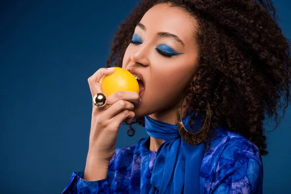 African american woman with makeup eating tasty lemon isolated on blue — Stock Photo