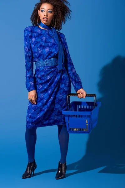 Mujer afroamericana sosteniendo cesta de la compra sobre fondo azul - foto de stock