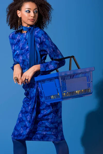 Afrikanisch-amerikanische Frau mit Einkaufskorb auf blauem Hintergrund — Stockfoto