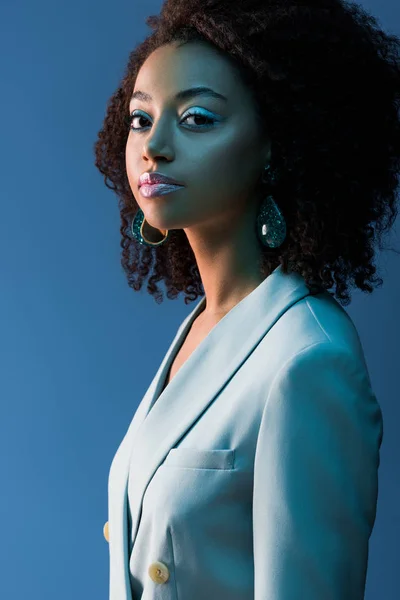 African american woman in jacket looking at camera isolated on blue — Stock Photo