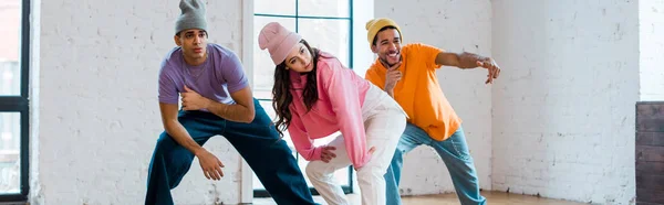 Panoramic shot of stylish multicultural dancers in hats breakdancing — Stock Photo
