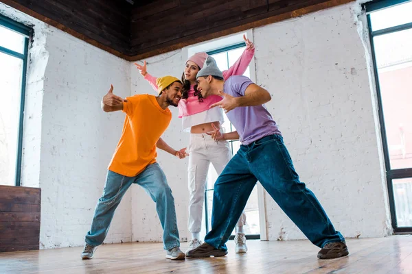 Hombres multiculturales gestos mientras breakdance con chica atractiva - foto de stock