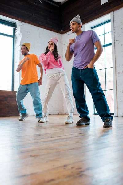 Guapos hombres multiculturales en sombreros breakdancing con chica atractiva - foto de stock