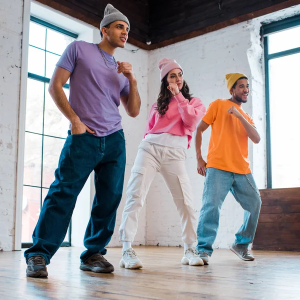 Hombres multiculturales con estilo en sombreros breakdancing con hermosa chica - foto de stock