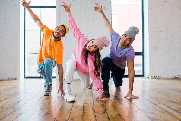 Homens multiculturais elegantes em chapéus breakdancing com atraente jovem mulher — Fotografia de Stock