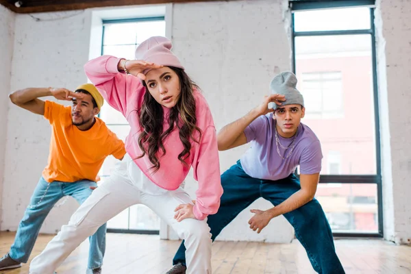 Foco seletivo de breakdancing menina elegante com homens multiculturais em chapéus — Fotografia de Stock