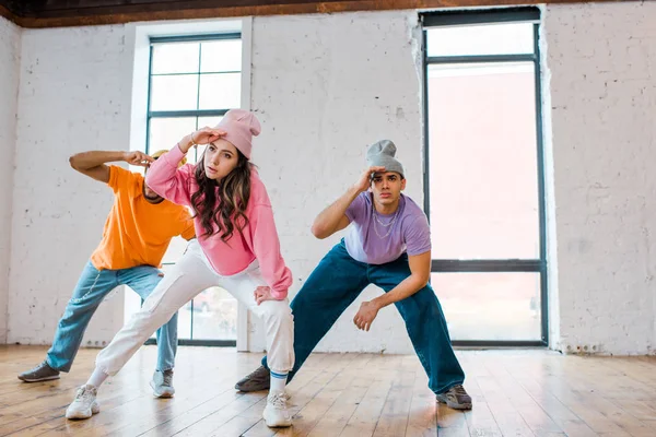 Stylish girl breakdancing with multicultural men in hats — Stock Photo