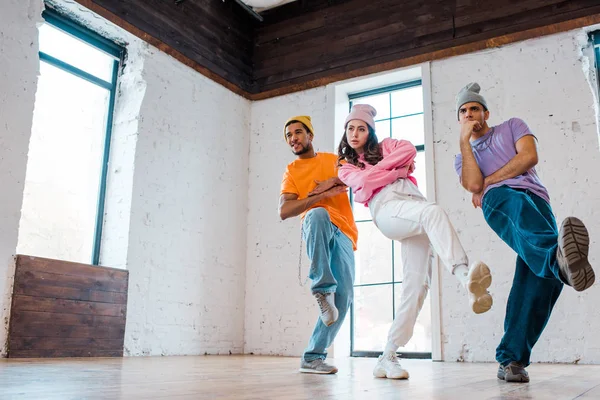 Stylish girl with crossed arms breakdancing with multicultural men in hats — Stock Photo